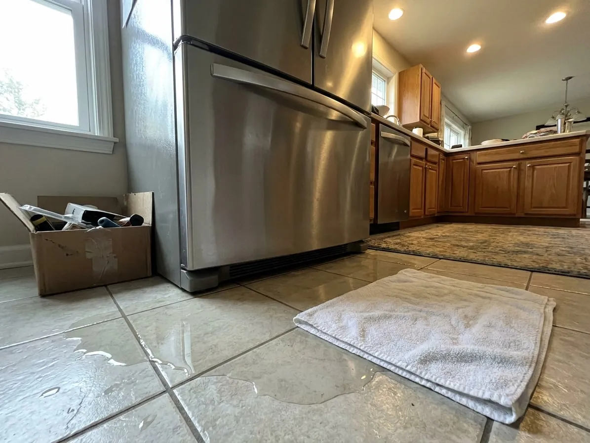 Puddle of water on a tile floor in front of a refrigerator freezer drawer